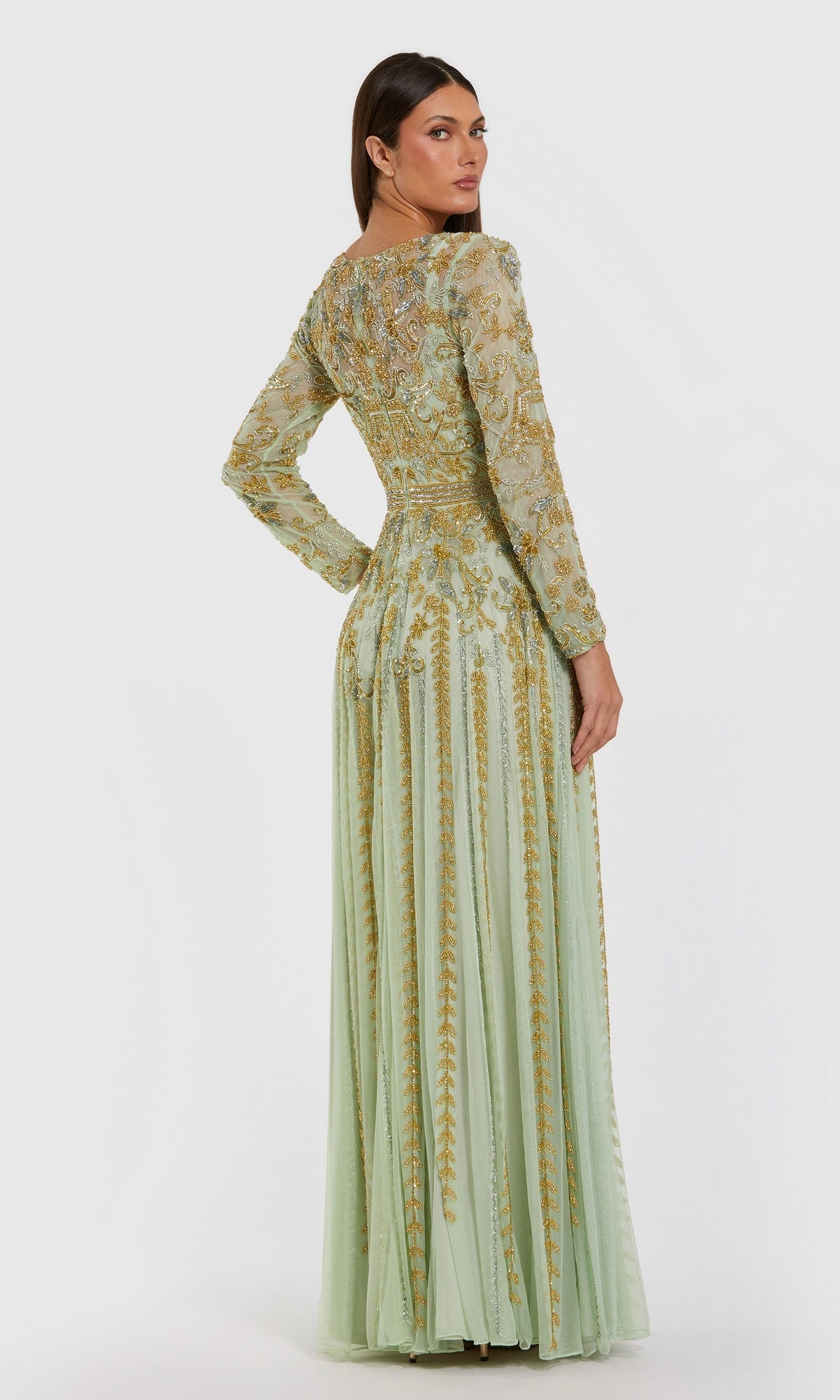 A woman stands facing away, showcasing the intricate back details of the Long Formal Dress: Mac Duggal 6201—a light green, modest formal gown adorned with gold embroidery and subtle gold beaded embellishments—set against a plain white background.